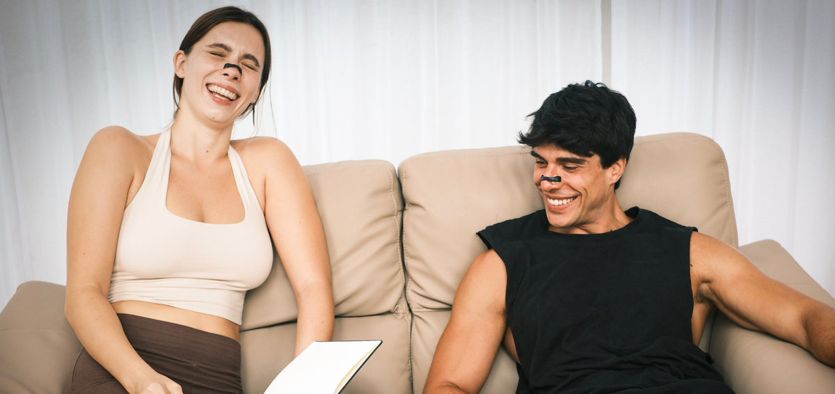 Two people relaxing on a sofa, both wearing an aira nasal strip